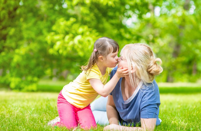 Kleines Mädchen mit Beeinträchtigungen küsst ihre Mutter auf einer Wiese.