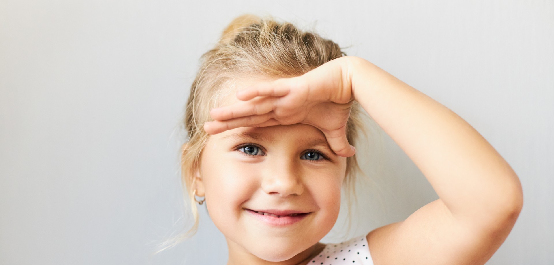 Kleines Mädchen mit blonden Haaren legt seine Handfläche auf die Stirn, als ob es in die Ferne schaut